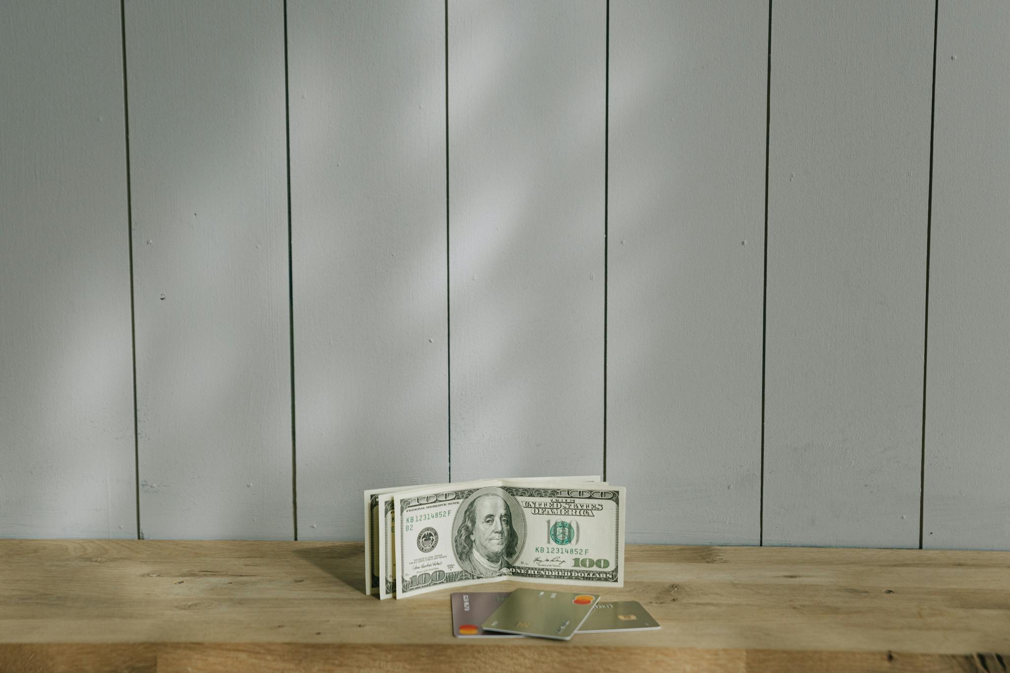 소액결제 현금화 A stack of hundred-dollar bills and credit cards on a wooden surface with a neutral background.