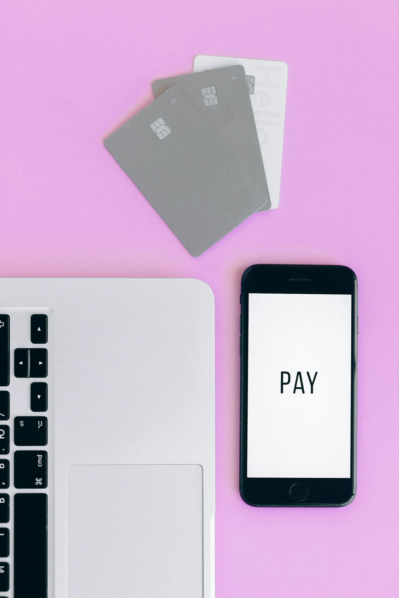 Top view of mobile payment 소액결제 현금화 setup with smartphone, credit cards, and laptop on pink background.